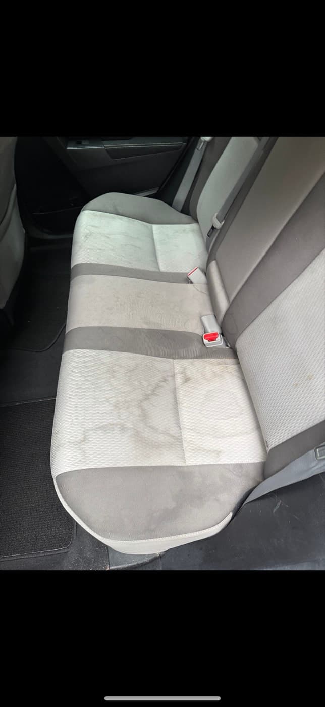 A grey fabric rear bench seat in a car, ground-in dirt across the base, before cleaning