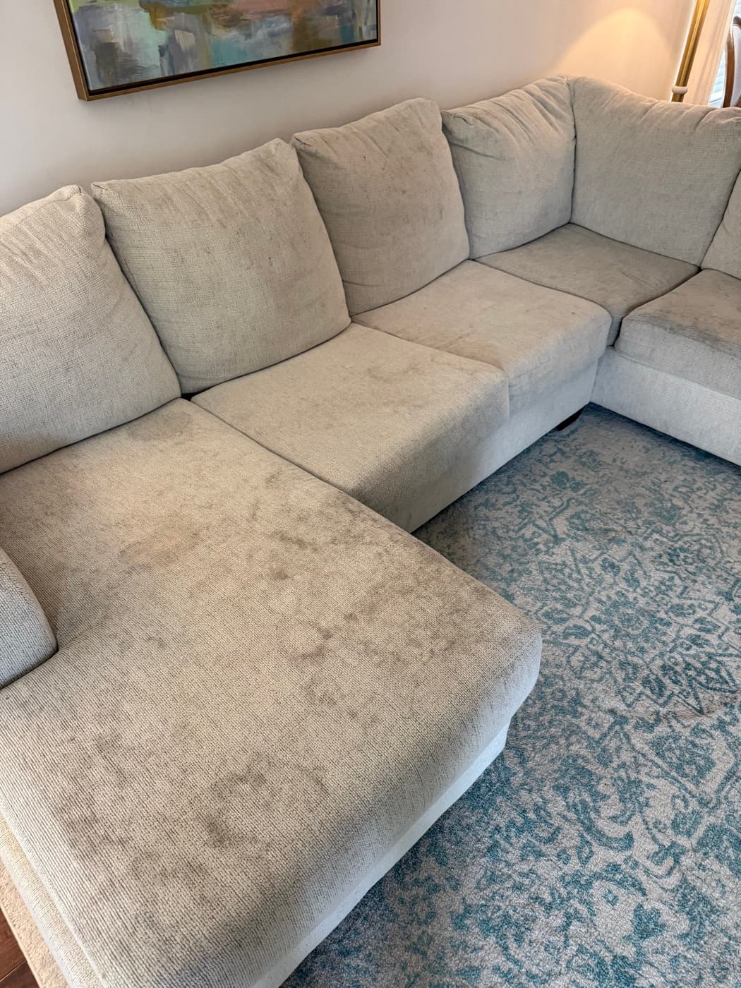 A light grey sectional sofa with dark marks worked into the chaise cushion, before cleaning