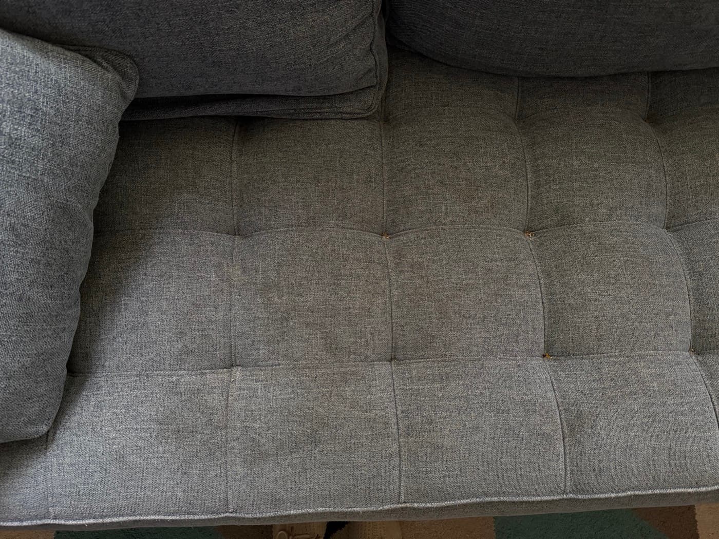 A grey tufted daybed, before cleaning