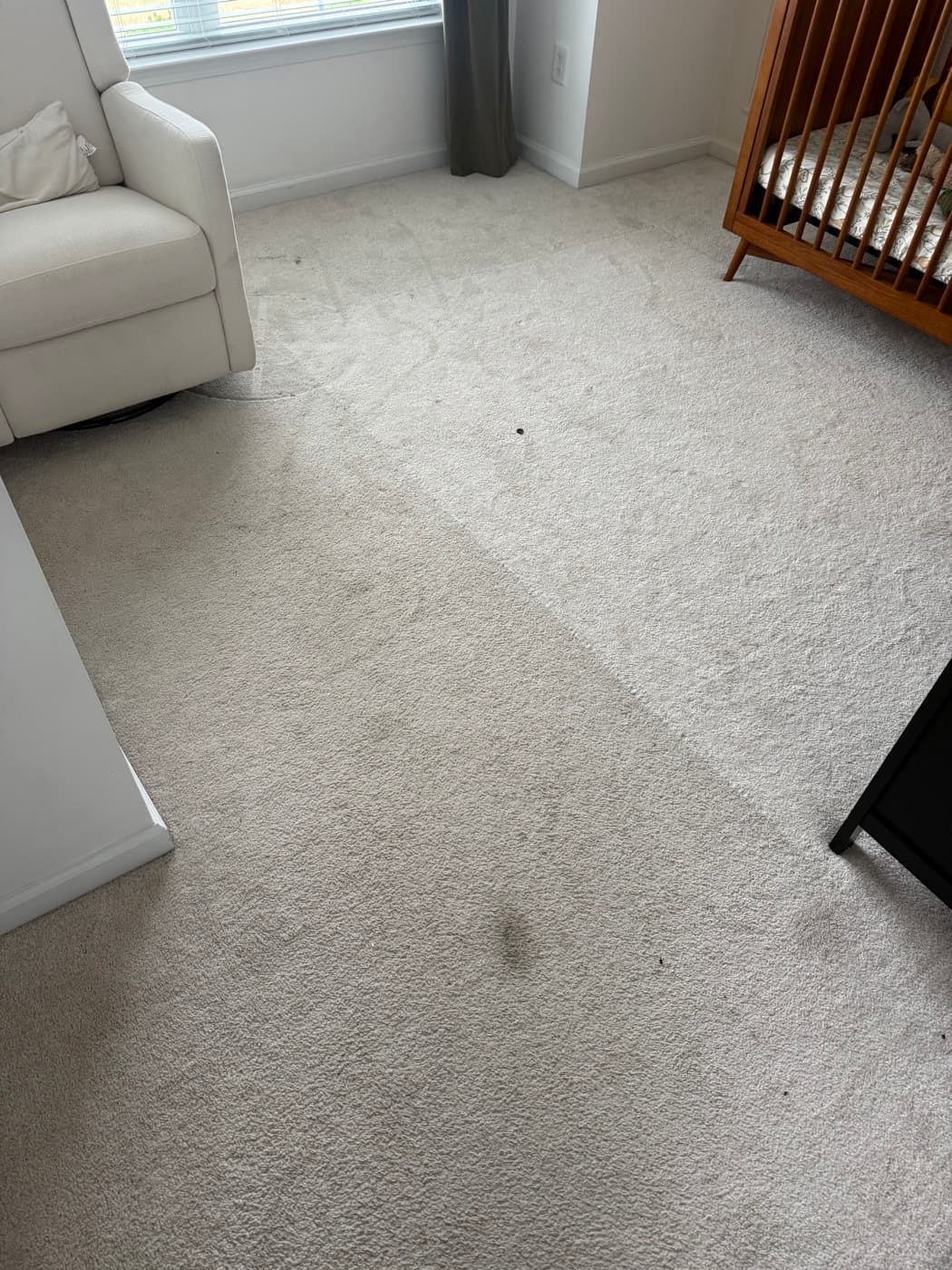 A bedroom carpet with dark stains along the side of the bed, before cleaning