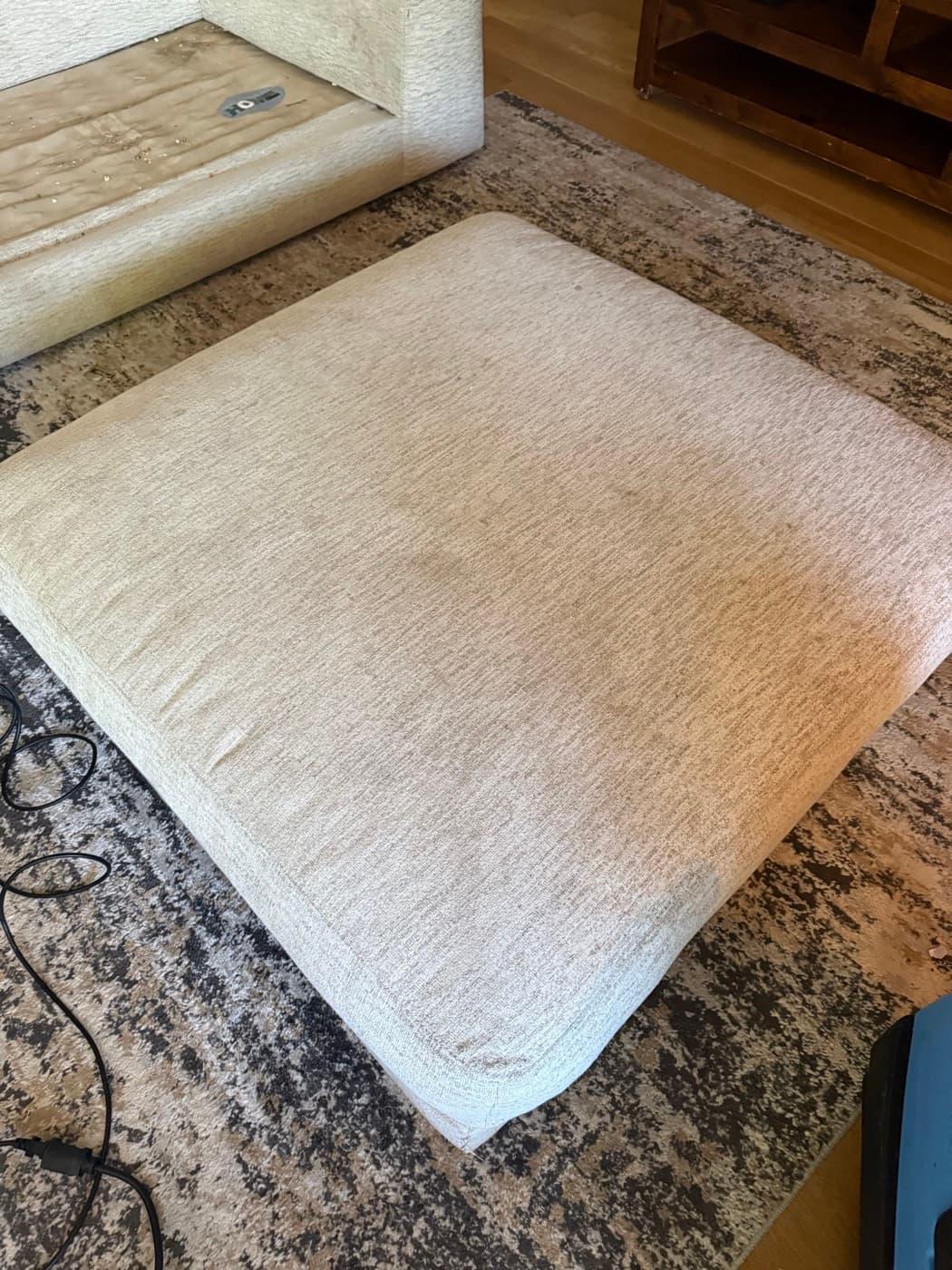 A large cream fabric ottoman with dull patches across the top, before cleaning