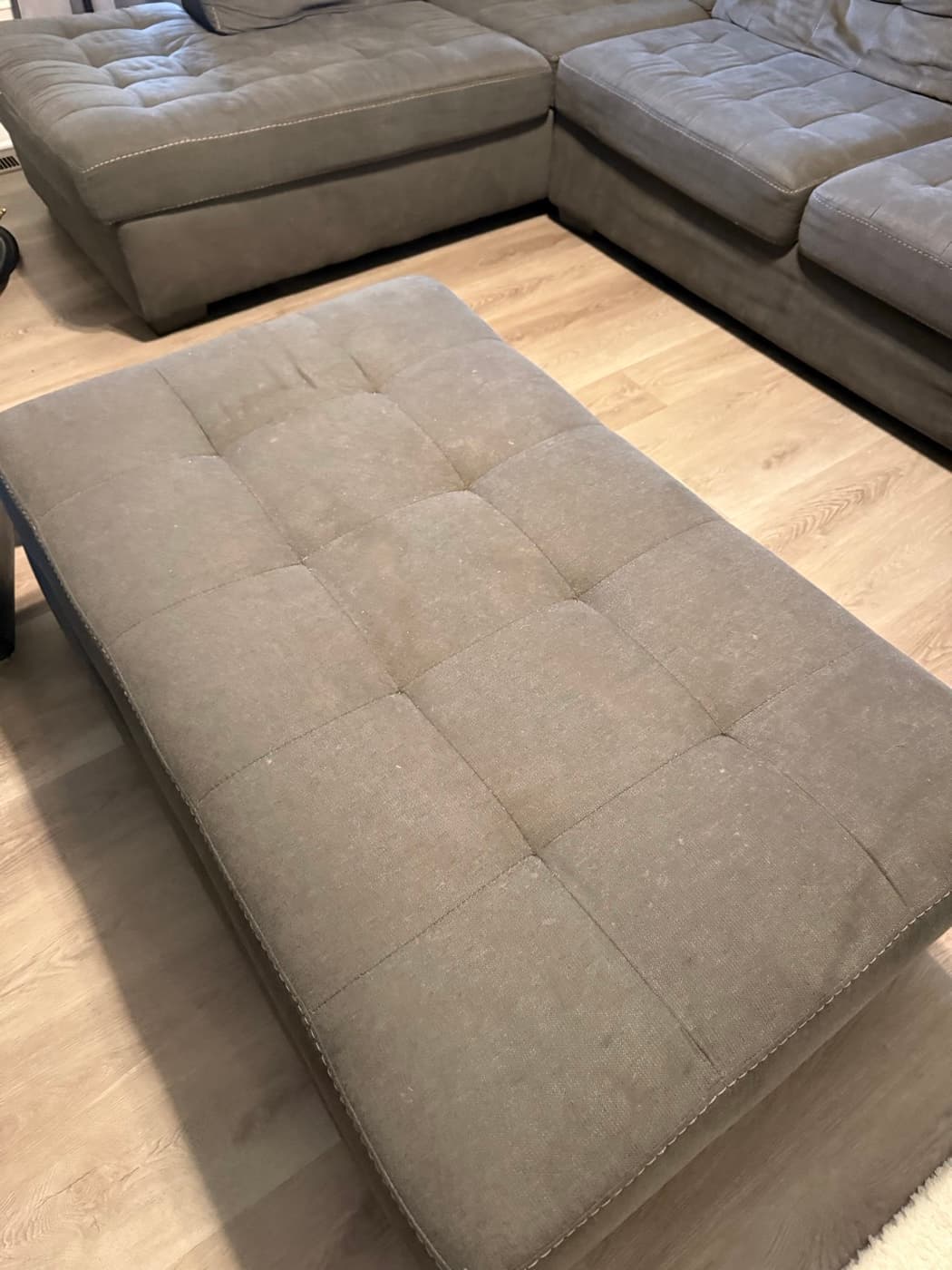 A beige tufted sofa bed, opened out flat, before cleaning