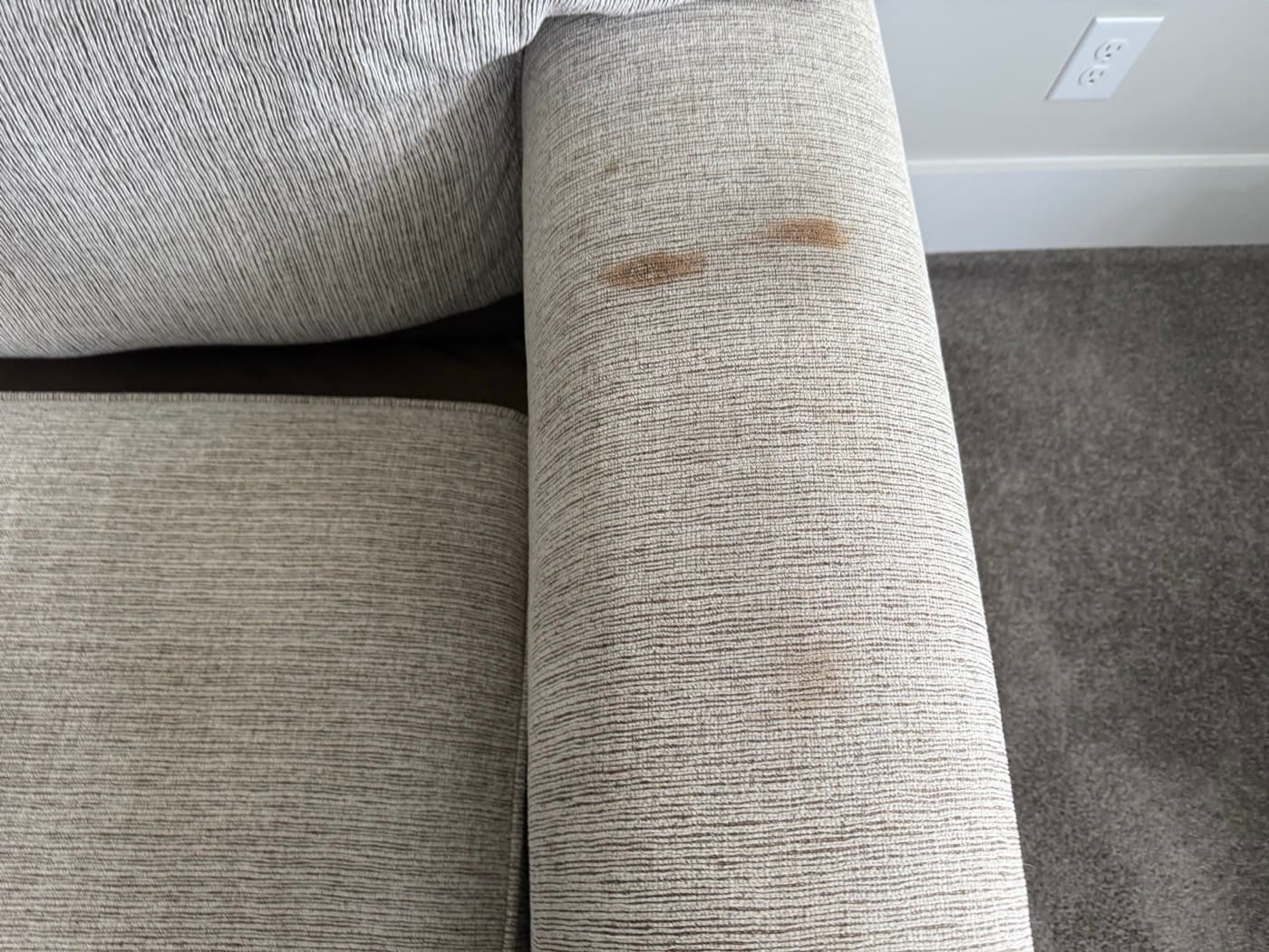 A grey sofa with a brown stain on the back cushion, before cleaning